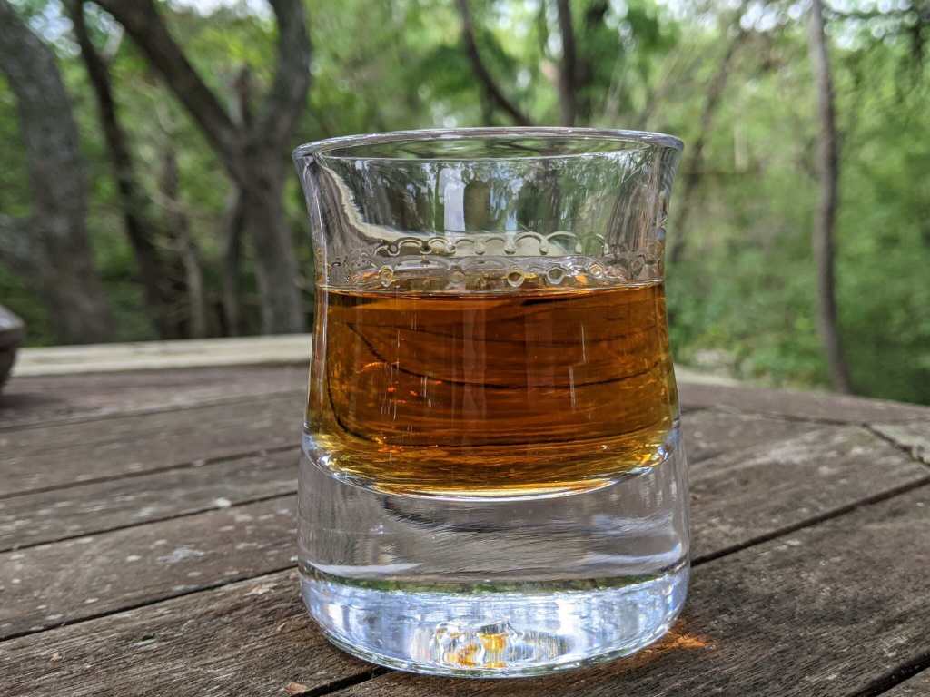 Whisky on Ice in a "rocks" glass on a wood table among trees